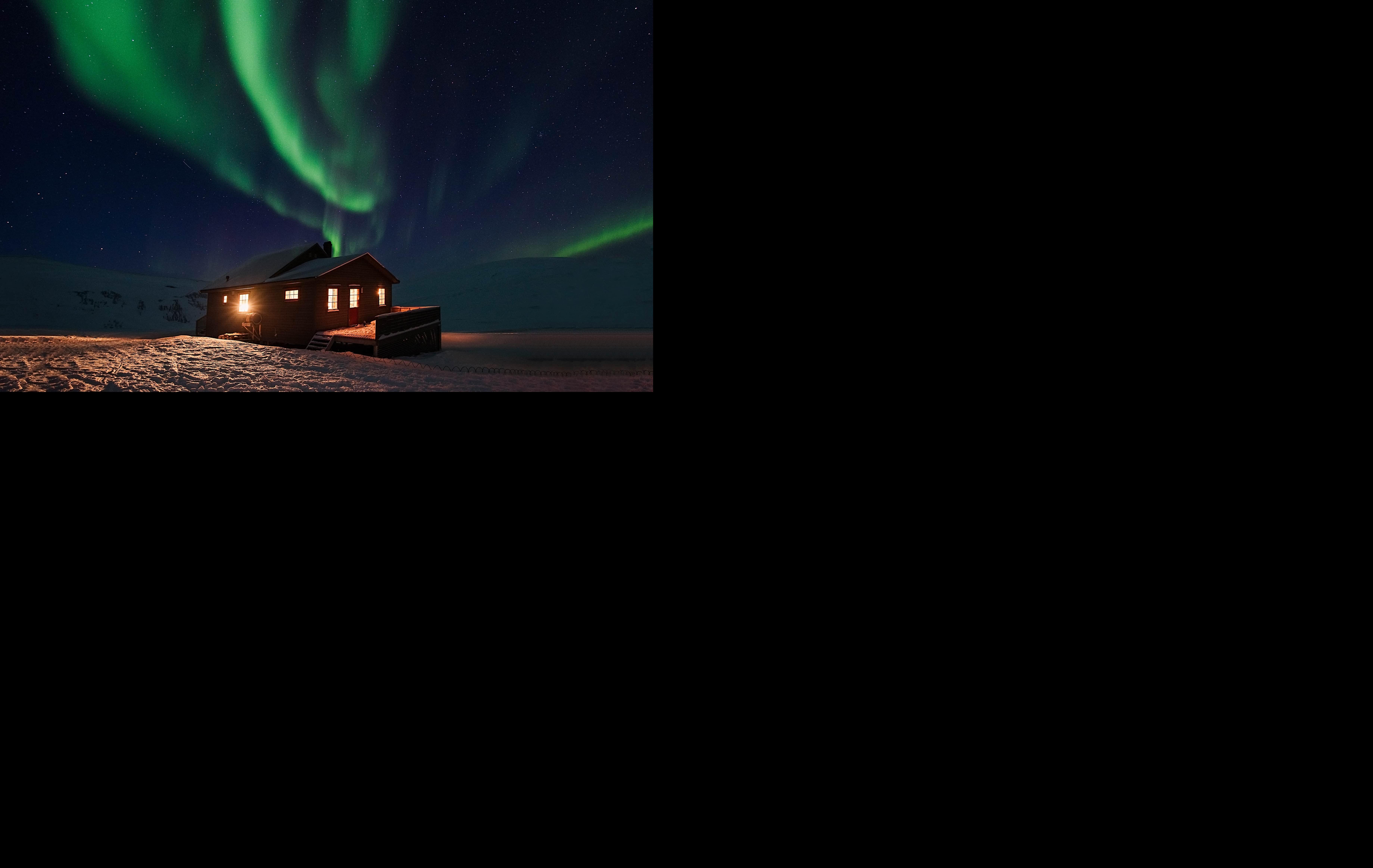 Arktis Tours Jenseits des Lichts: Polarnacht auf Spitzbergen - Polarlicht über einer einsamen Hütte