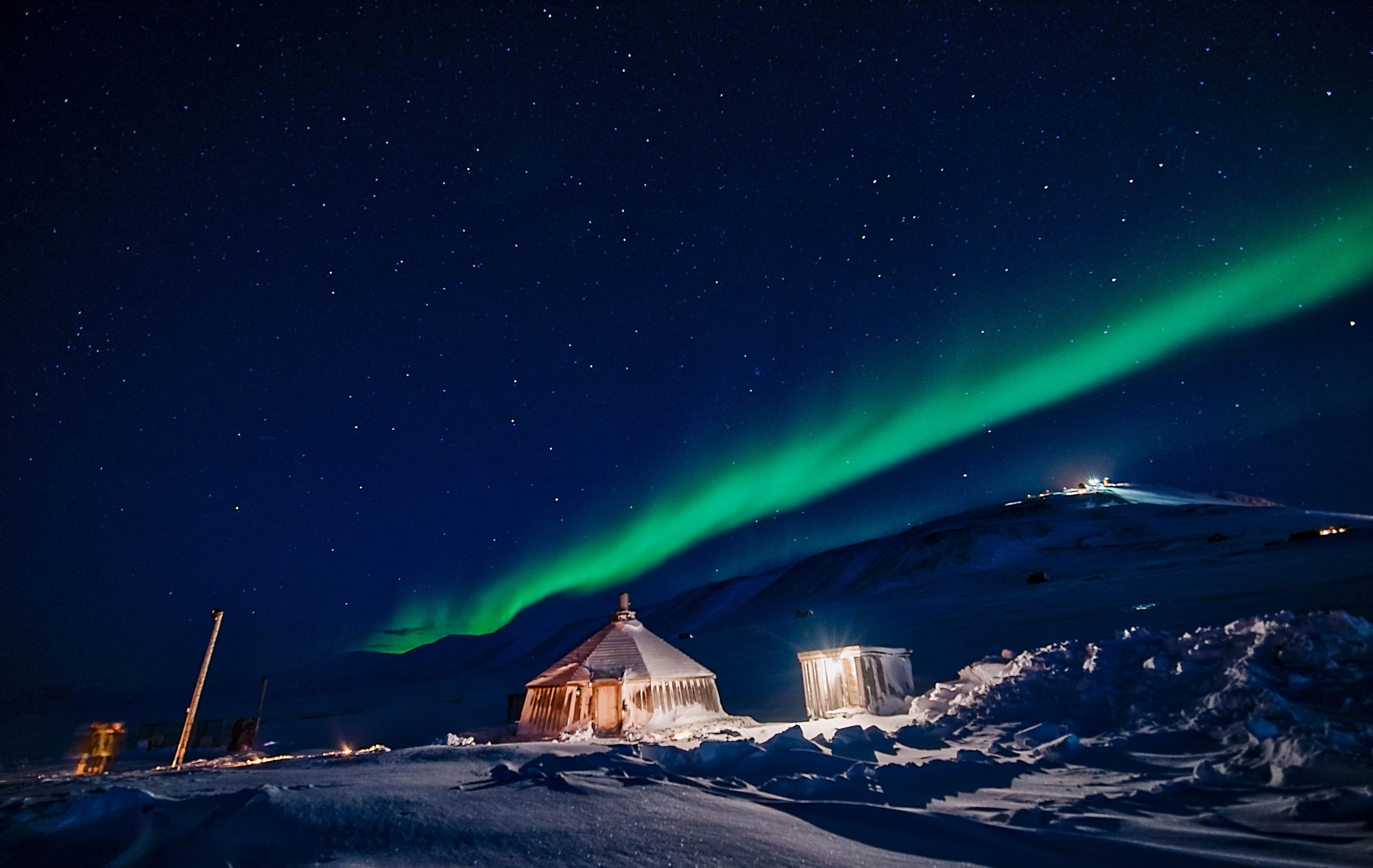 Arktis Tours Jenseits des Lichts: Polarnacht auf Spitzbergen - Polarlicht über einer einsamen Hütte