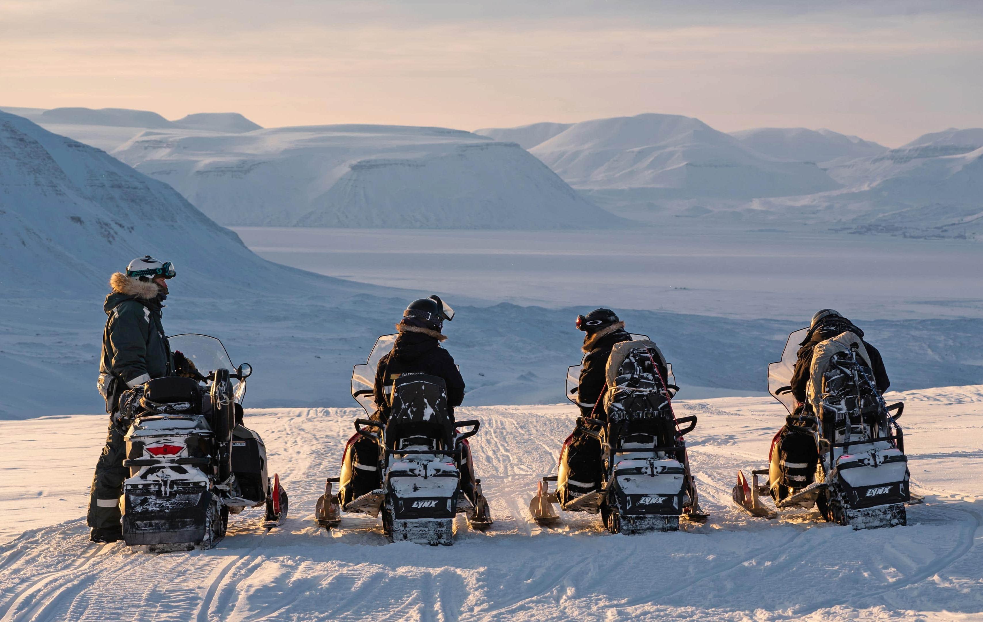 Arktis Tours Grenzgang im Eis: Snowmobil-Expedition West-Spitzbergen - Gruppe von Snowmobil Fahrern blickt über die gebirgige Landschaft
