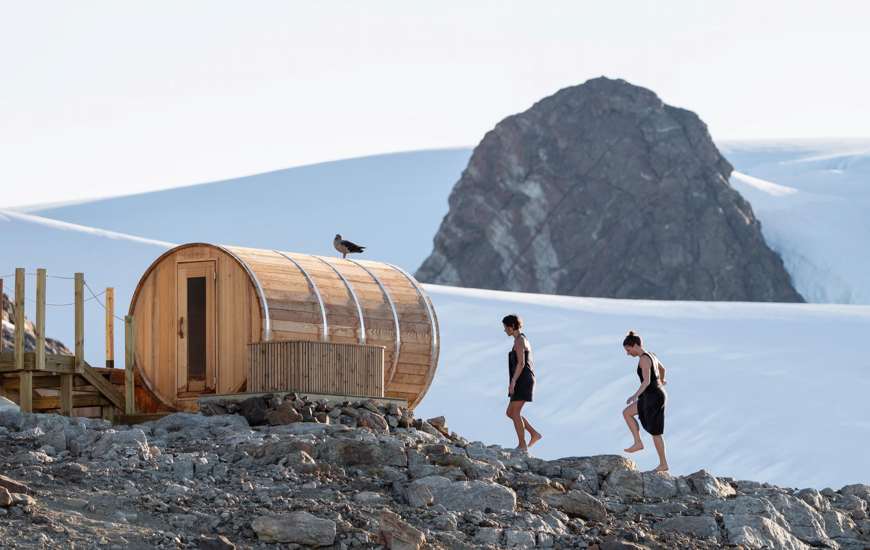 Arktis Tours - Südpol in Sicht: Antarktisreise de Luxe - Zwei Personen vor einer Fass-Sauna inmitten des Eises der Antarktis